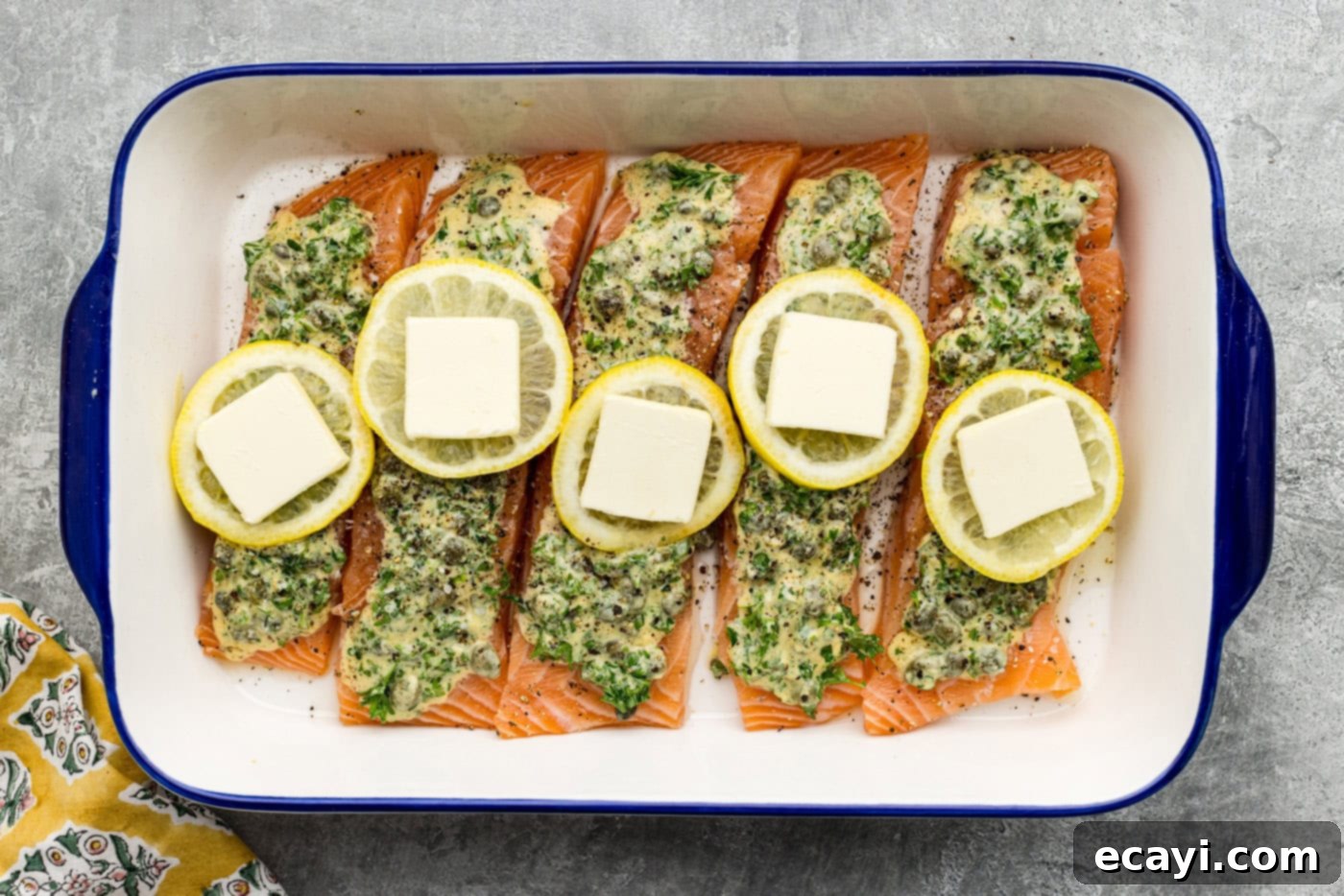 Zesty Lemon Caper Salmon 7 butt pats placed on top of lemon slices over raw lemon caper salmon in a dish