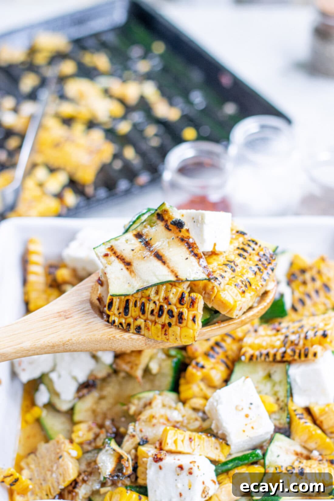 Grilled Corn, Zucchini and Feta Salad 3 Serving a portion of Grilled Corn & Zucchini Salad with Feta from a large bowl.
