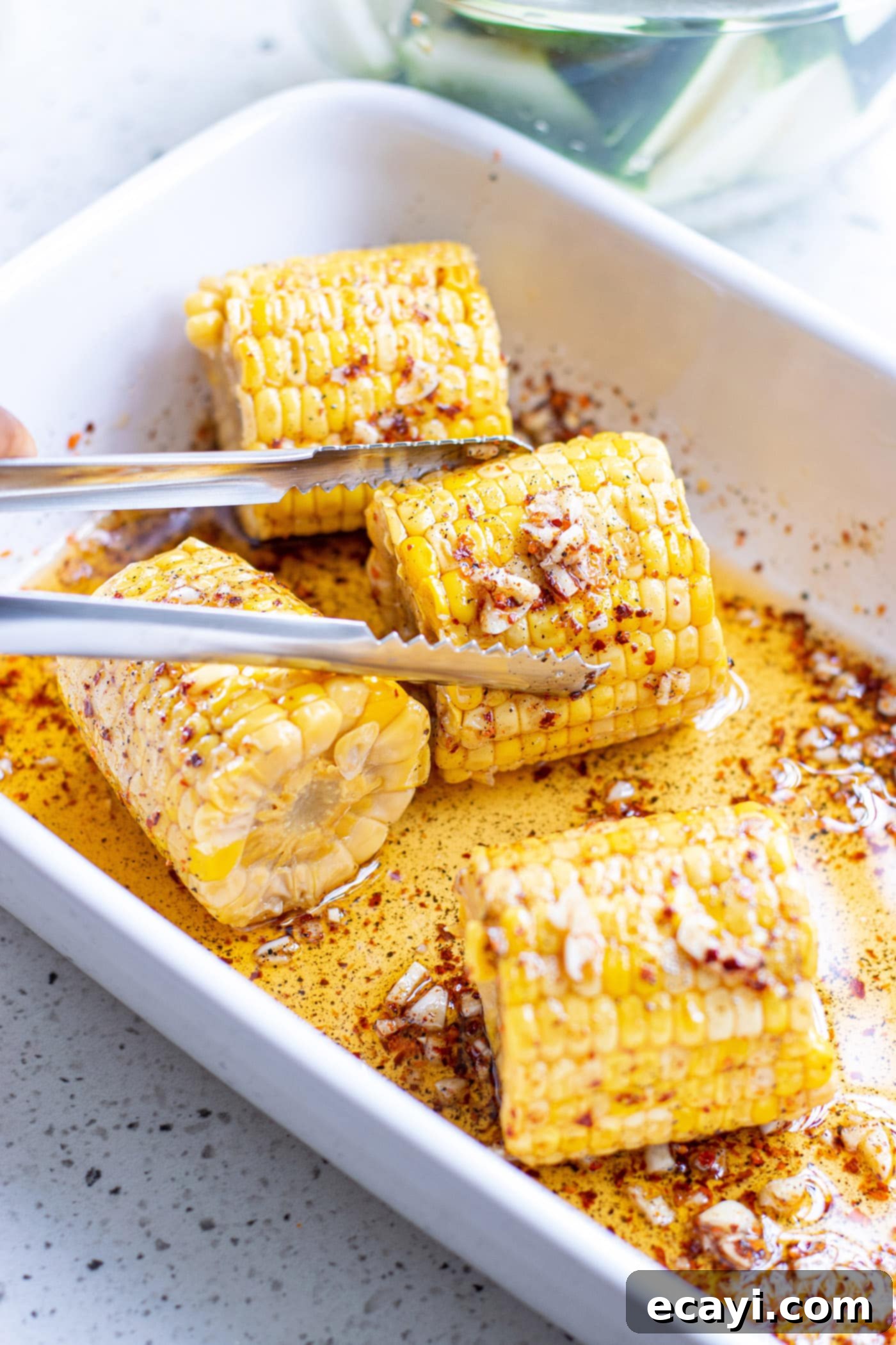 Grilled Corn, Zucchini and Feta Salad 7 Tongs holding an ear of corn coated in marinade.