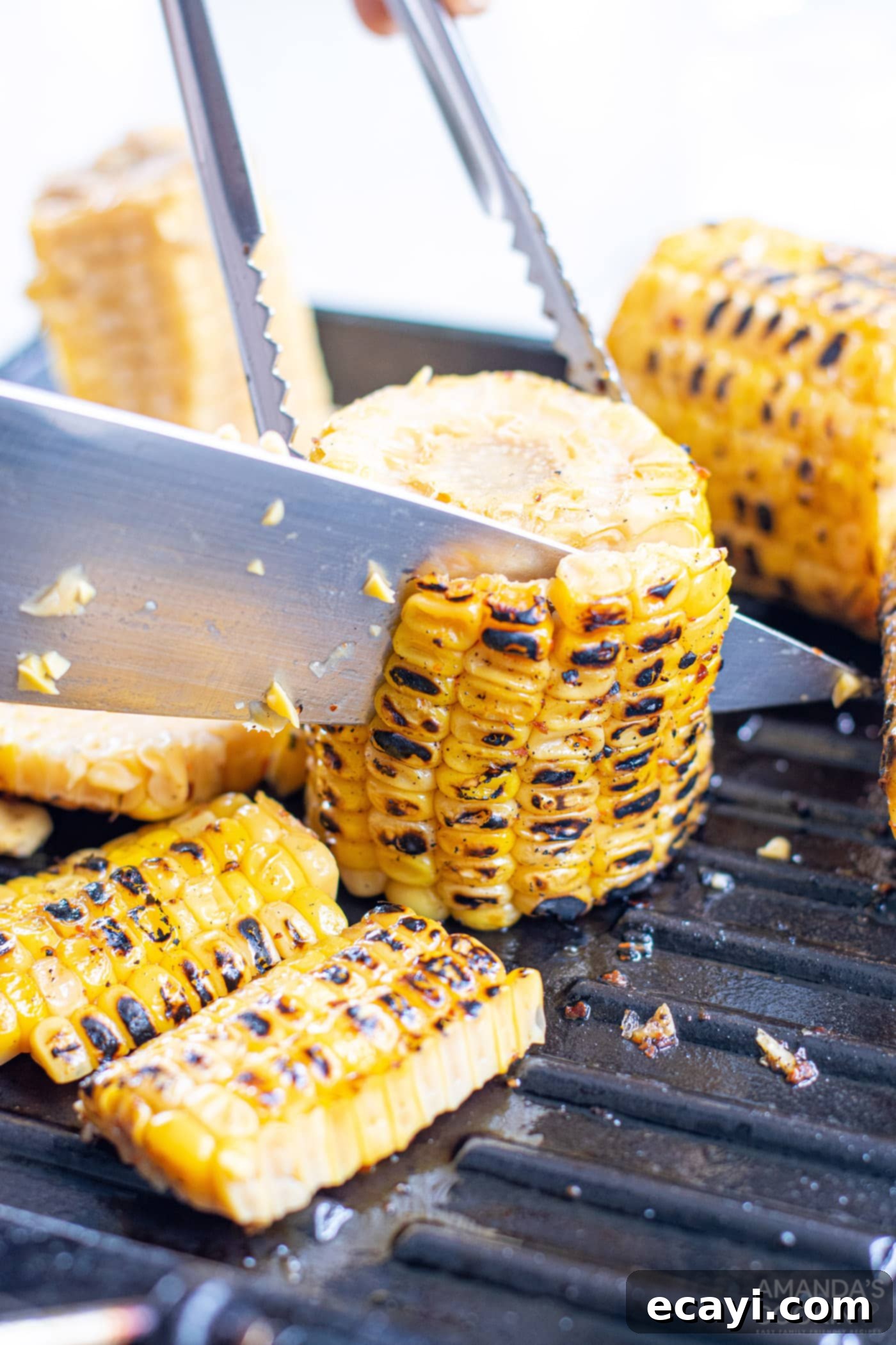 Grilled Corn, Zucchini and Feta Salad 10 A knife slicing corn kernels off the cob on a cutting board.