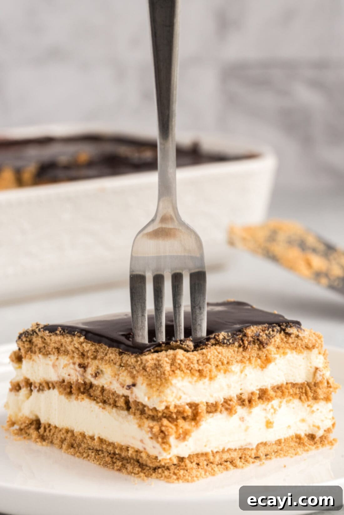 Decadent Eclair Delight 2 fork stuck into a slice of no-bake eclair cake showing layers of graham crackers, creamy filling, and chocolate ganache