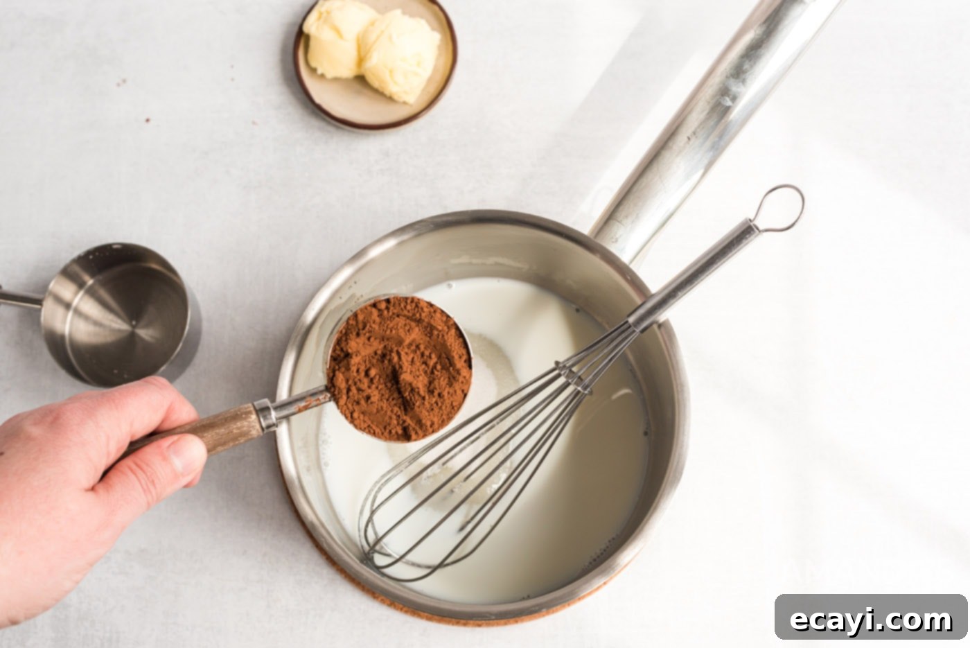 Decadent Eclair Delight 11 cocoa powder in a measuring cup held over a saucepan of milk and sugar, with whisking in progress