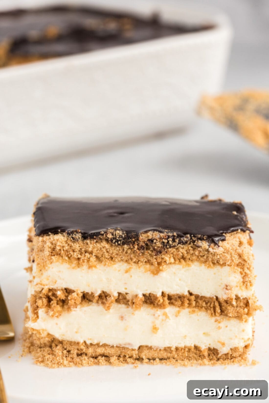 Decadent Eclair Delight 15 A perfectly sliced piece of eclair cake on a white plate, showing all the layers and a fork