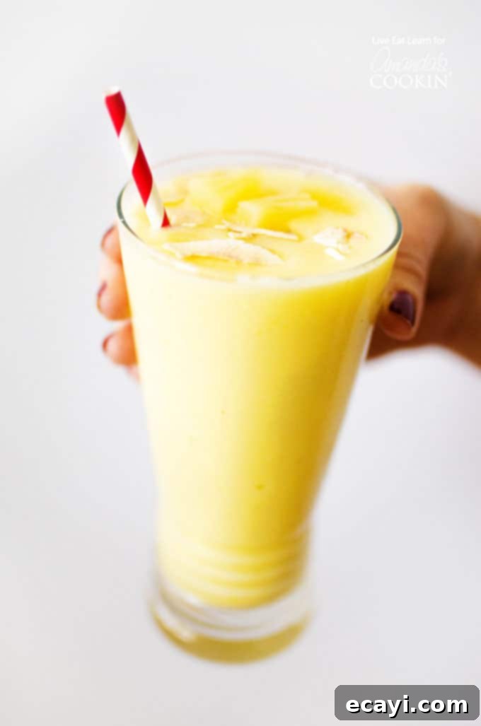 Pina Colada Paradise Smoothie 2 Pina Colada Smoothie Drink Recipe, showing a tall glass filled with a creamy yellow smoothie, garnished with a pineapple wedge and shredded coconut.