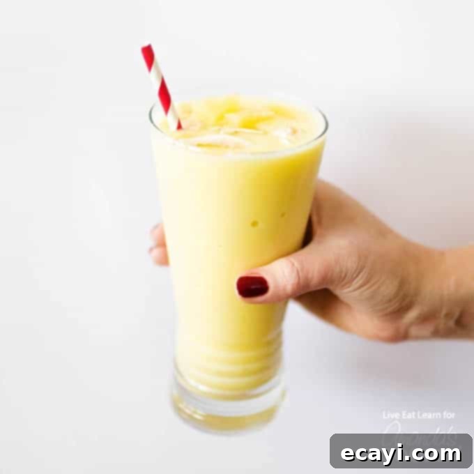Pina Colada Paradise Smoothie 3 Hand holding a glass of Pina Colada Smoothie, garnished with a tiny paper umbrella.