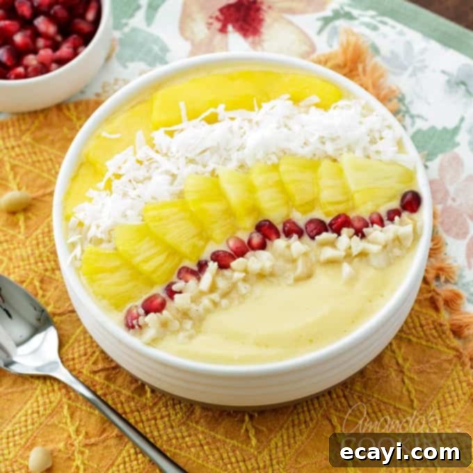 This refreshing tropical smoothie bowl is bursting with flavor and reminds me of a bowl of sunshine! This smoothie bowl is perfect for summer. #tropical #smoothie #smoothiebowl #breakfast #fruit #dairyfree #mango #peach #coconut Close up of a tropical smoothie bowl with layered garnishes including pomegranate, coconut, pineapple, and mango