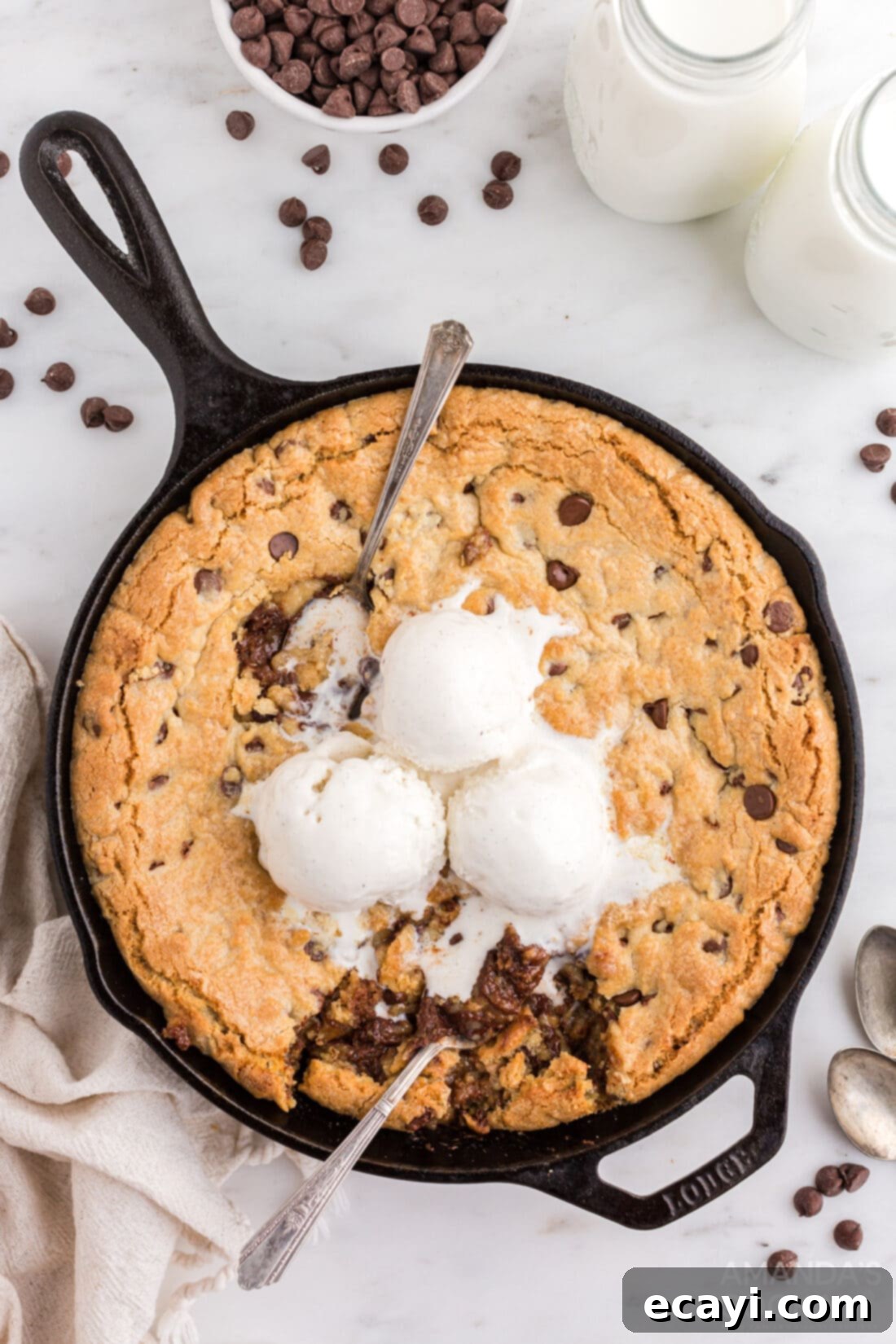 Decadent Skillet Chocolate Chip Cookie 10 Large chocolate chip cookie in a cast iron skillet with several scoops of vanilla ice cream melting on top, ready to be eaten.