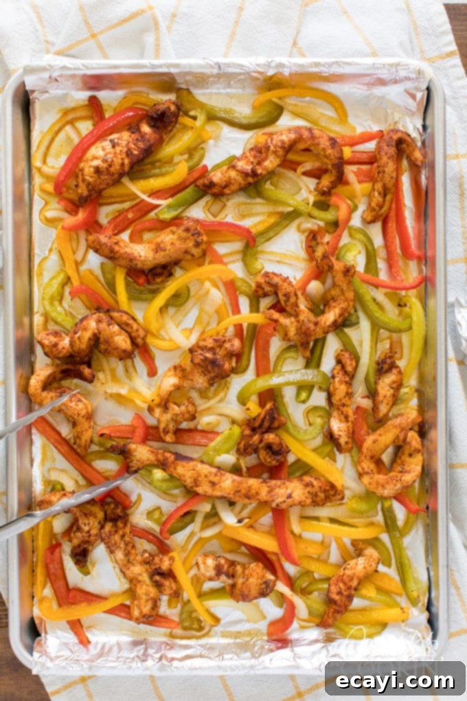 One-Pan Chicken Fajitas 4 Foil-lined sheet pan with seasoned chicken strips, bell peppers, and onions before cooking
