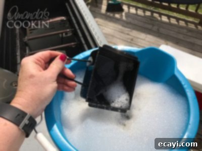 The Gas Grill Deep Clean: Restore Its Shine & Performance 16 dropping grease catcher from grill into soapy water to soak
