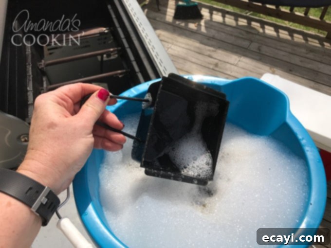 The Gas Grill Deep Clean: Restore Its Shine & Performance 6 dropping grease catcher from grill into soapy water to soak