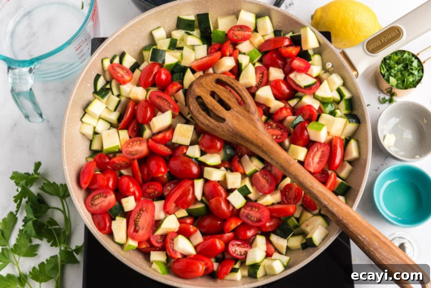 Summer Zucchini Tomato Pasta 5 Diced zucchini and halved grape tomatoes cooking gently in a skillet with melted butter and olive oil, with a wooden spoon for stirring.