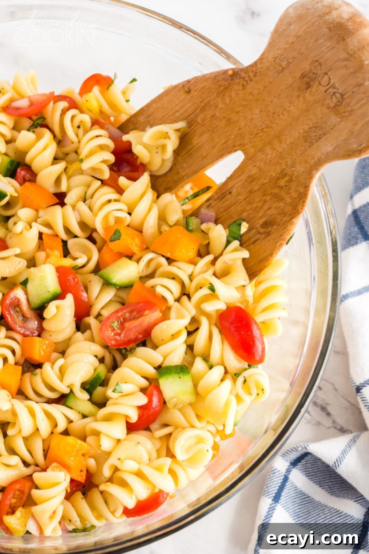 Minimal dressing ingredients and maximum fresh vegetables, this summer pasta salad will be the hit of your summer parties and holiday get togethers. Wooden fork in bowl of summer pasta salad, showcasing fresh vegetables and rotini