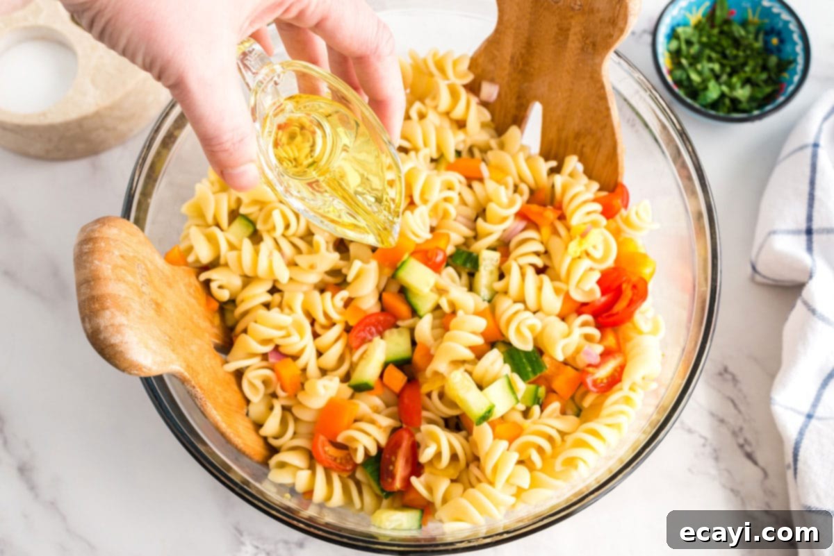 Refreshing Summer Pasta Salad 5 Pouring olive oil over the colorful pasta and vegetable mixture in a large bowl