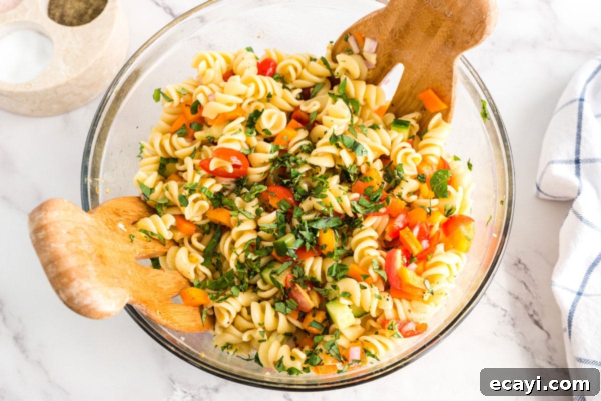 Minimal dressing ingredients and maximum fresh vegetables, this summer pasta salad will be the hit of your summer parties and holiday get togethers. Freshly chopped basil being sprinkled over the finished summer pasta salad in a bowl