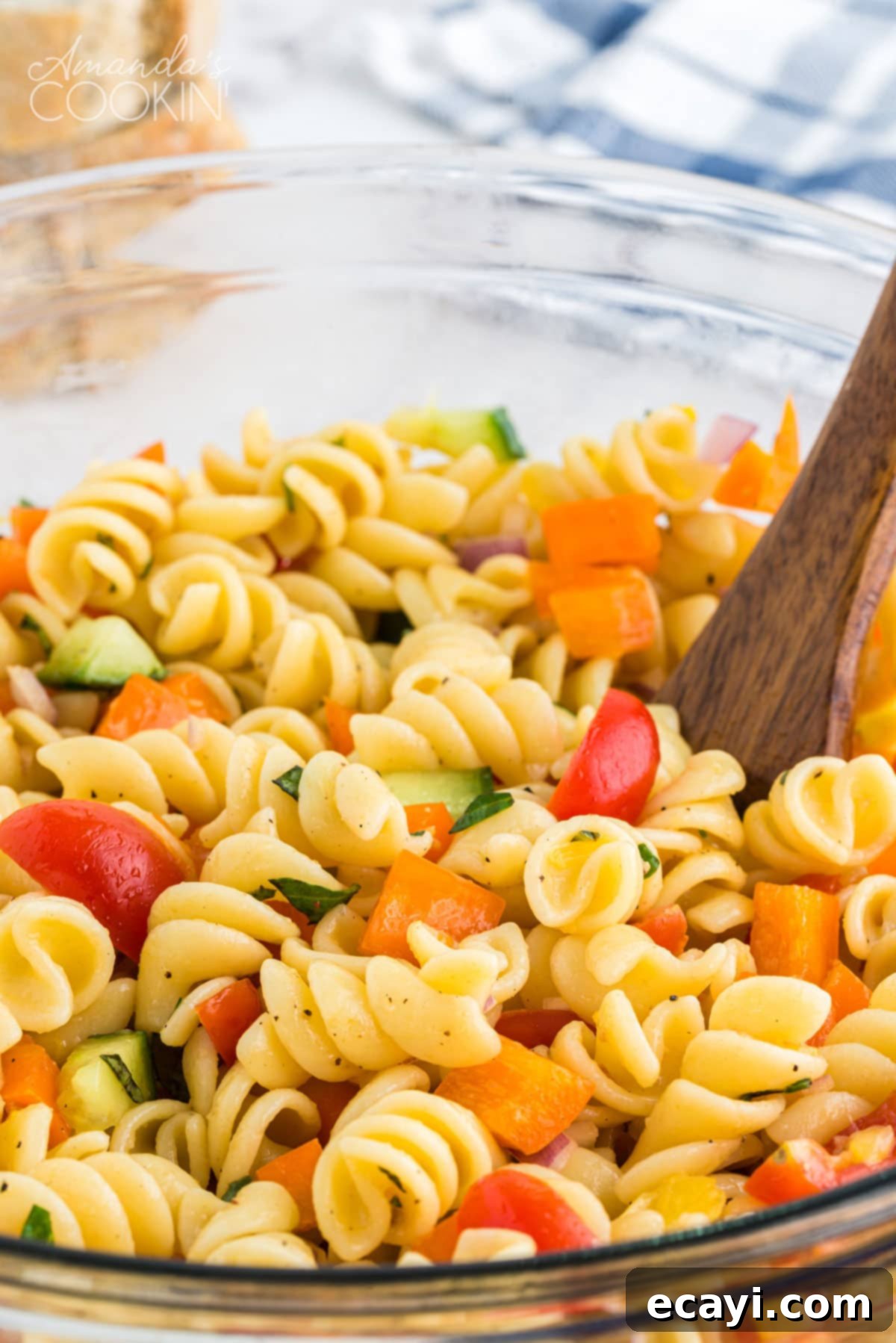 Minimal dressing ingredients and maximum fresh vegetables, this summer pasta salad will be the hit of your summer parties and holiday get togethers. Close-up of vibrant summer pasta salad in a white bowl with a wooden spoon, ready to be served