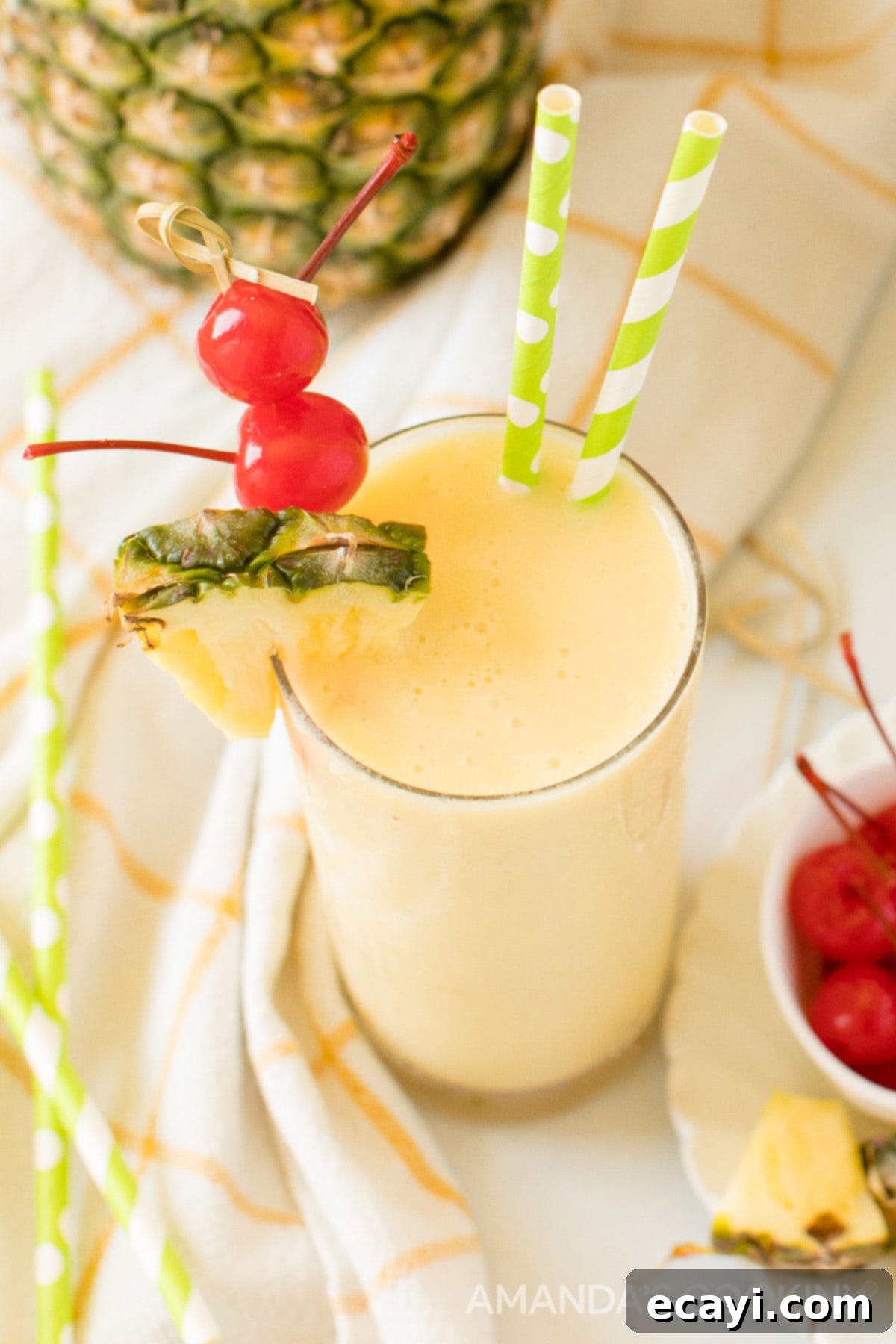 With only 3 ingredients, this pineapple rum slush is one of our favorite frozen rum drinks! A quick cocktail that's perfect for a crowd on a hot summer day. Glass of Pineapple Rum Slush garnished with cherries and pineapple wedge, with green and white straws