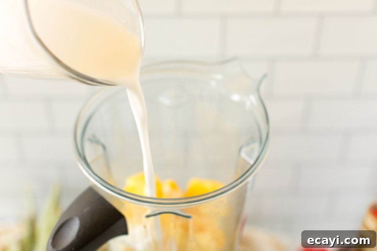 Tropical Rum Slushy 3 Pouring coconut milk into a blender with frozen pineapple