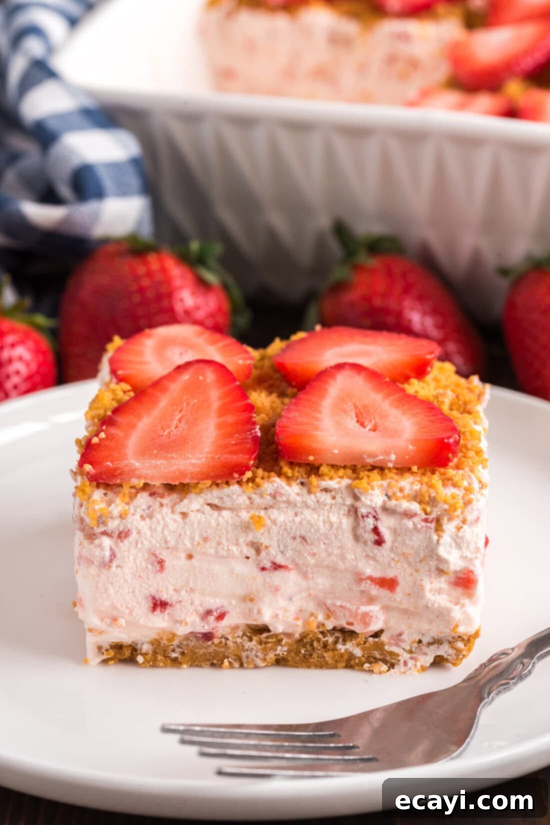 Blush Berry Bliss 2 A delectable slice of Strawberry Dream Dessert on a plate, ready to be enjoyed with a fork. The creamy layers and fresh strawberries are clearly visible.
