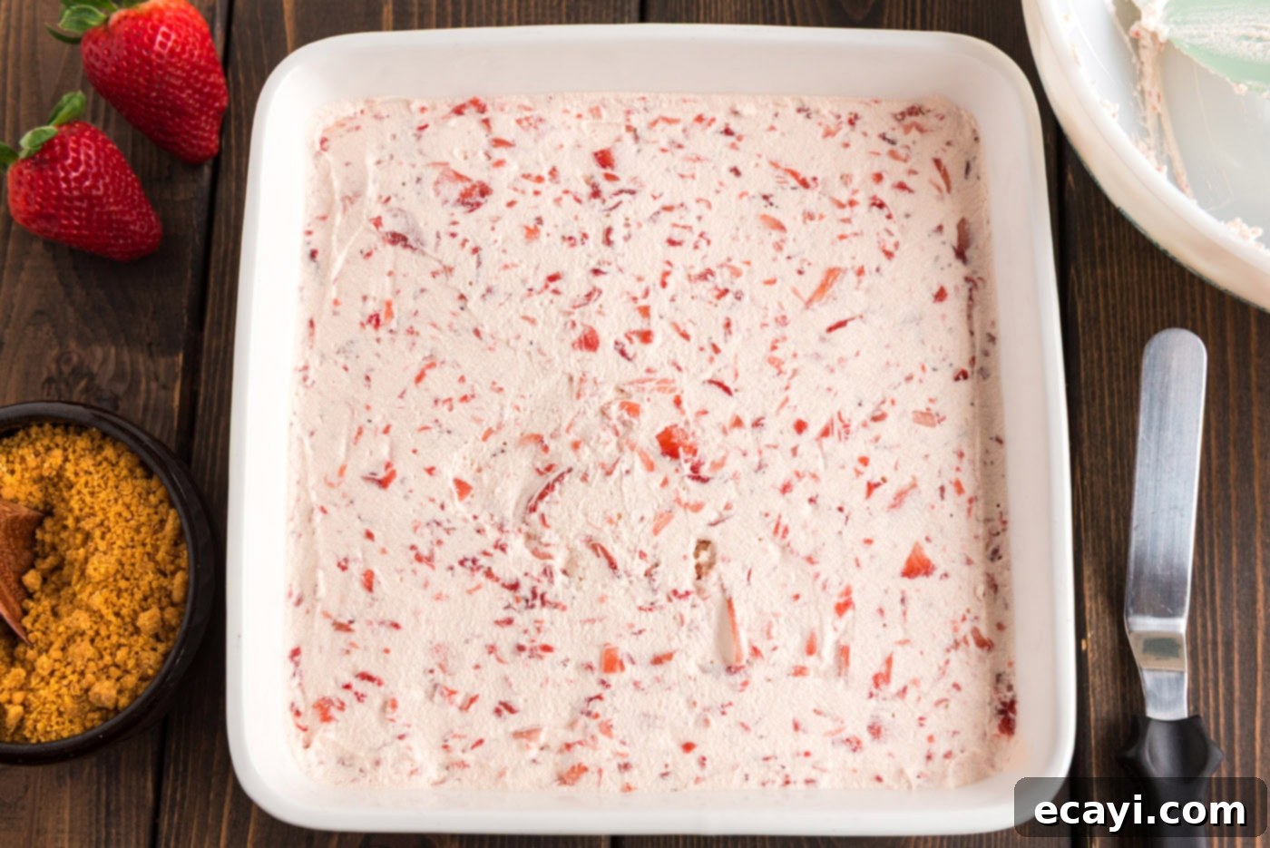 Blush Berry Bliss 11 The strawberry Cool Whip mixture being spread over the cream cheese layer in the pan, forming the final topping.