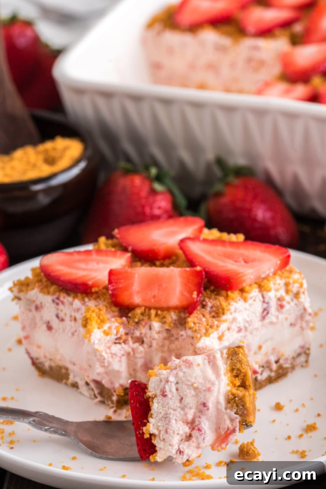 Blush Berry Bliss 3 A fork holding a bite of Strawberry Dream Dessert, with a full slice resting in the background. Shows the layers of crust, cream, and strawberries.