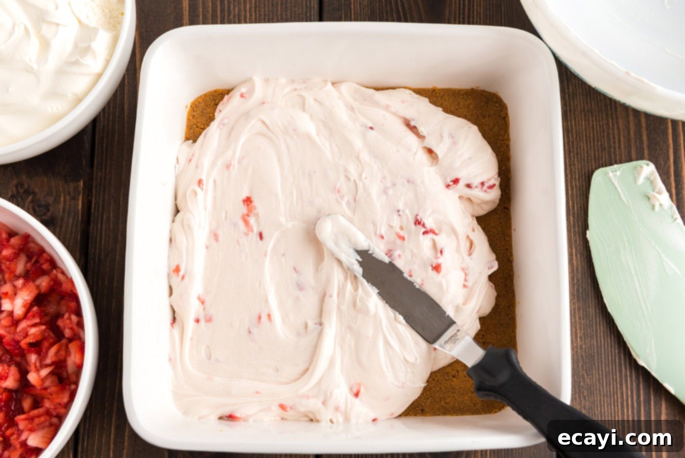 Blush Berry Bliss 9 A rubber spatula spreading the strawberry cream cheese filling evenly over the graham cracker crust in the pan.
