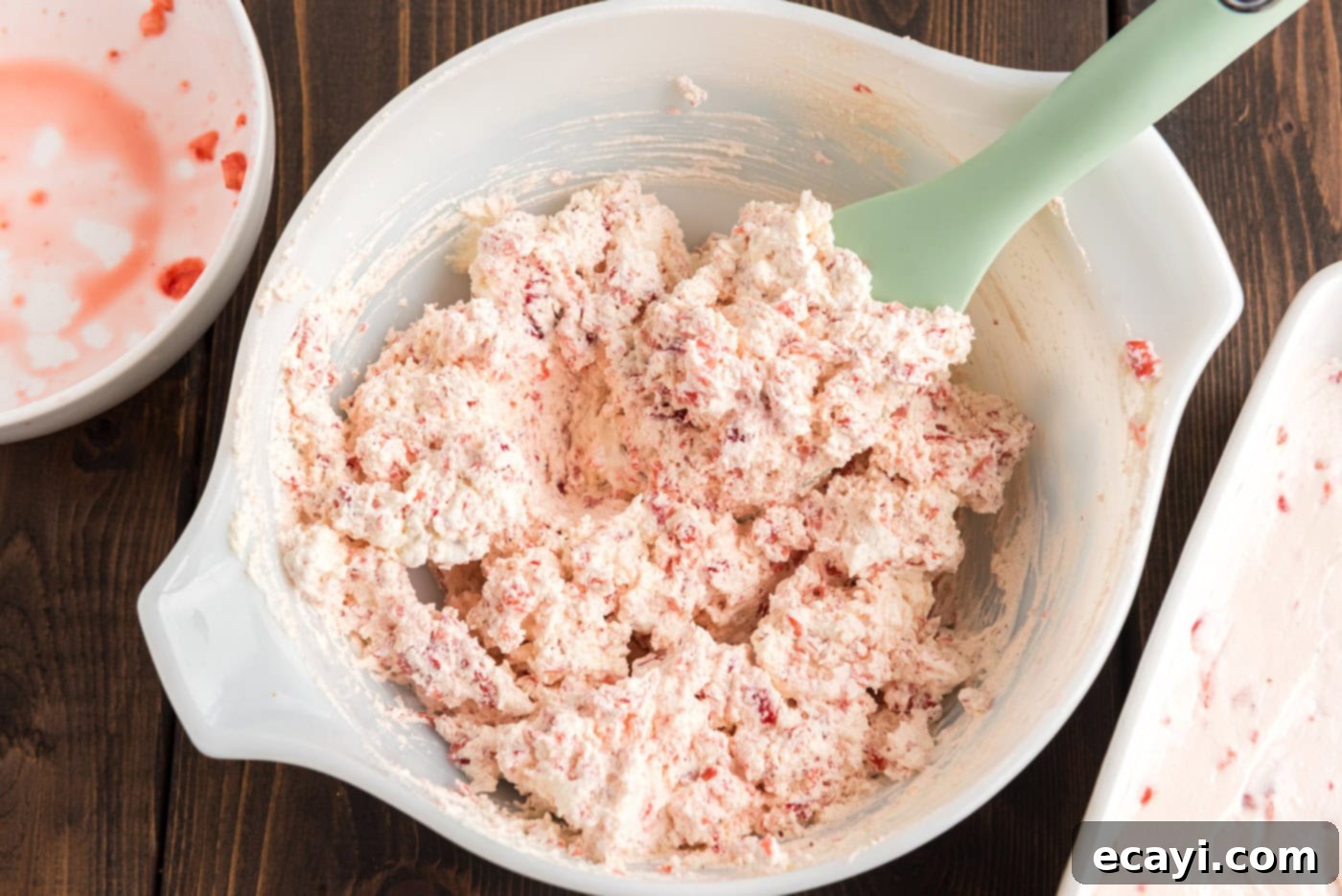 Blush Berry Bliss 10 Cool Whip mixed with strawberry chunks in a bowl, creating a light pink and fruity topping.