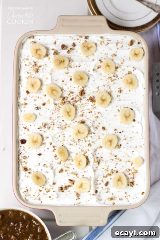 Freshly prepared Banana Cream Lush in a baking pan, ready for chilling. Layered banana dessert topped with fresh bananas in a baking pan