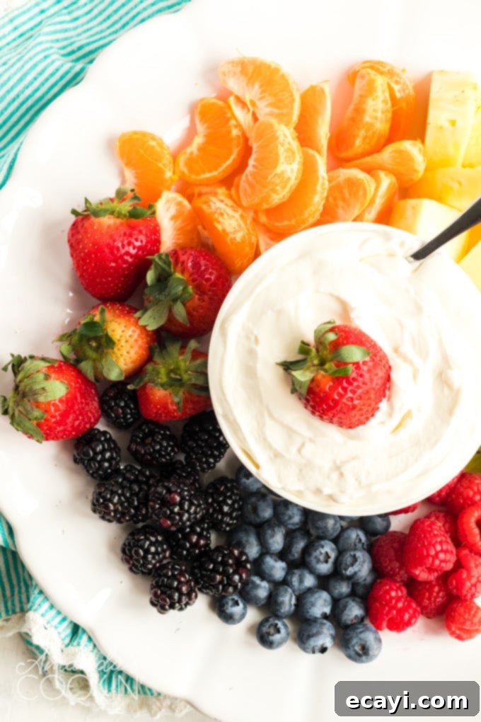 This Cream Cheese Fruit Dip is a really cool way to sneak in lots of fresh fruit on hot summer days. It's sweet and fluffy- perfect with any summer fruit! #fruit #fruitdip #dip #diprecipes #appetizers #creamcheese #strawberries #summer #football A beautifully arranged white plate full of colorful fresh fruit with a bowl of fluffy cream cheese fruit dip in the center, ready to be enjoyed.