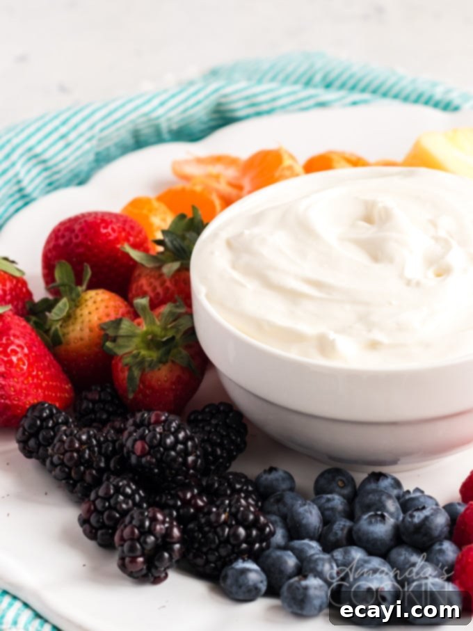 This Cream Cheese Fruit Dip is a really cool way to sneak in lots of fresh fruit on hot summer days. It's sweet and fluffy- perfect with any summer fruit! #fruit #fruitdip #dip #diprecipes #appetizers #creamcheese #strawberries #summer #football A white bowl filled with creamy, fluffy cream cheese fruit dip, perfectly smooth and ready for dipping.