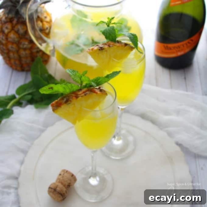 This Pineapple Prosecco Punch is bursting with pineapple, white rum, mango juice, Prosecco and a hint of mint. Perfect for sipping and relaxing! #cocktail #brunch #summercocktails #summerdrinks #partydrinks #prosecco #pineapple #wine #rum #brunchcocktail Close-up of Pineapple Prosecco Punch in elegant champagne flutes, showcasing the golden color and delicate bubbles, garnished with pineapple.