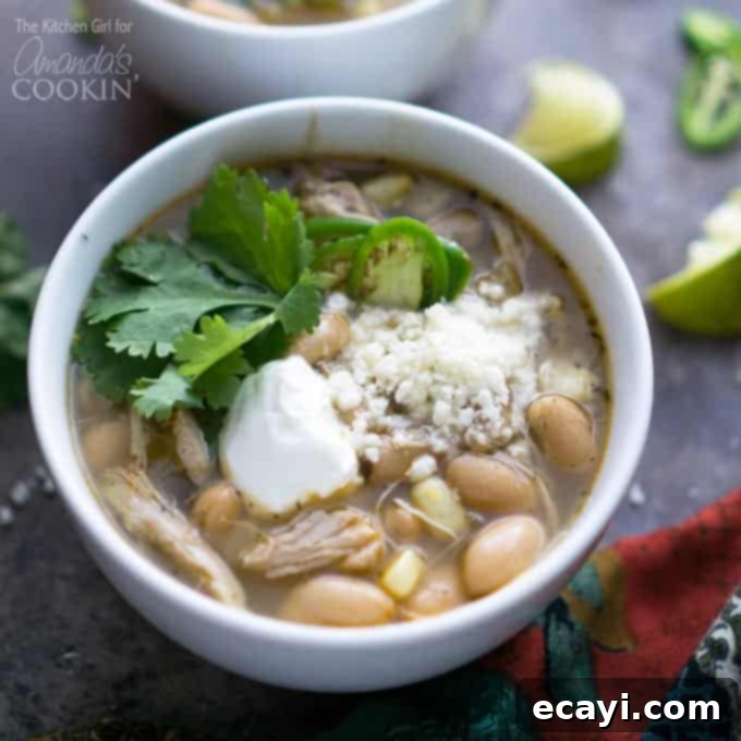 This white chicken chili is incredibly easy to make in a slow cooker, featuring tender chicken and rich, spicy flavors. #chickenrecipes #chicken #chili #whitechickenchili #crockpot #slowcooker #crockpotrecipes #crockpotsoup #soup #souprecipes Closeup of a bowl of creamy white chicken chili, garnished with fresh cilantro and a dollop of sour cream