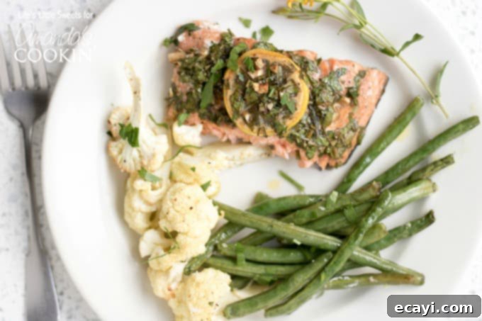You'll love this easy and flavorful Sheet Pan Salmon Dinner with lemon and tarragon! A single serving of Sheet Pan Salmon Dinner artfully arranged on a plate, featuring a salmon fillet, roasted green beans, and cauliflower, garnished with fresh herbs and lemon.
