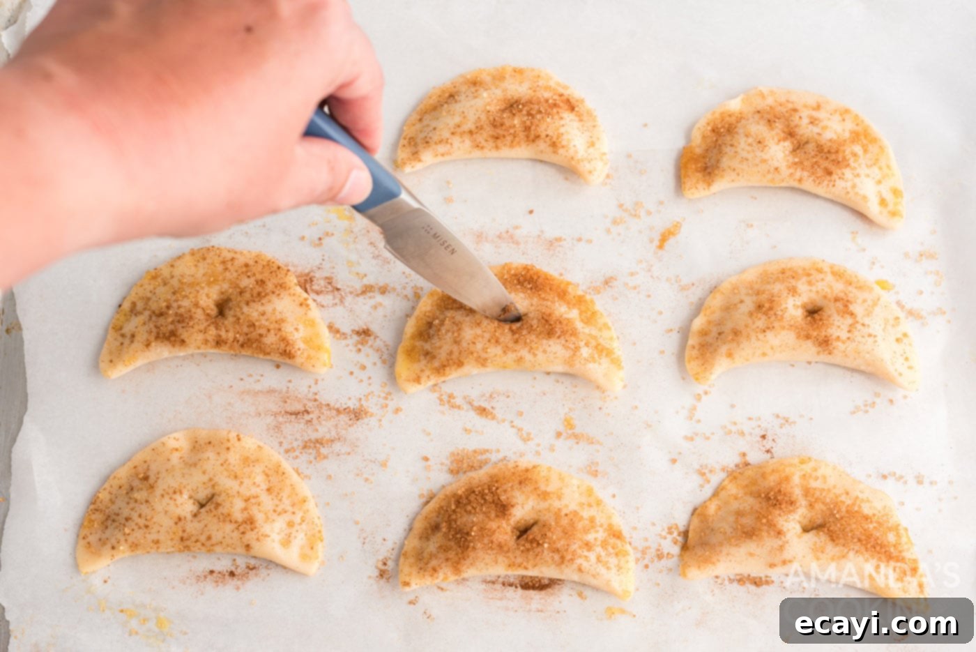 Flaky Pumpkin Turnovers 11 A knife cutting a small vent slit into the top of an unbaked pumpkin hand pie on a baking sheet.
