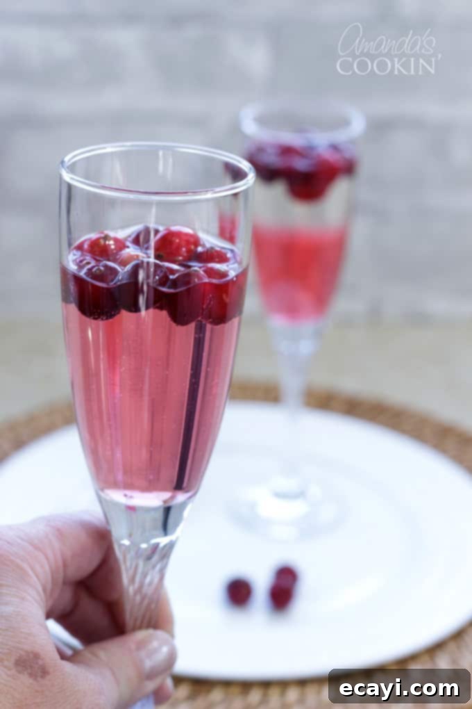 This Cranberry Prosecco Punch is great for Thanksgiving or Christmas morning, for your New Year's eve celebration, or enjoy on a crisp evening around a campfire with friends. #cranberry #prosecco #alcoholicdrinks #cocktails #partydrinks #falldrinks #christmascocktails #newyearsdrinks #newyearsevedrinks a hand holding a champagne flute filled with cranberry prosecco punch
