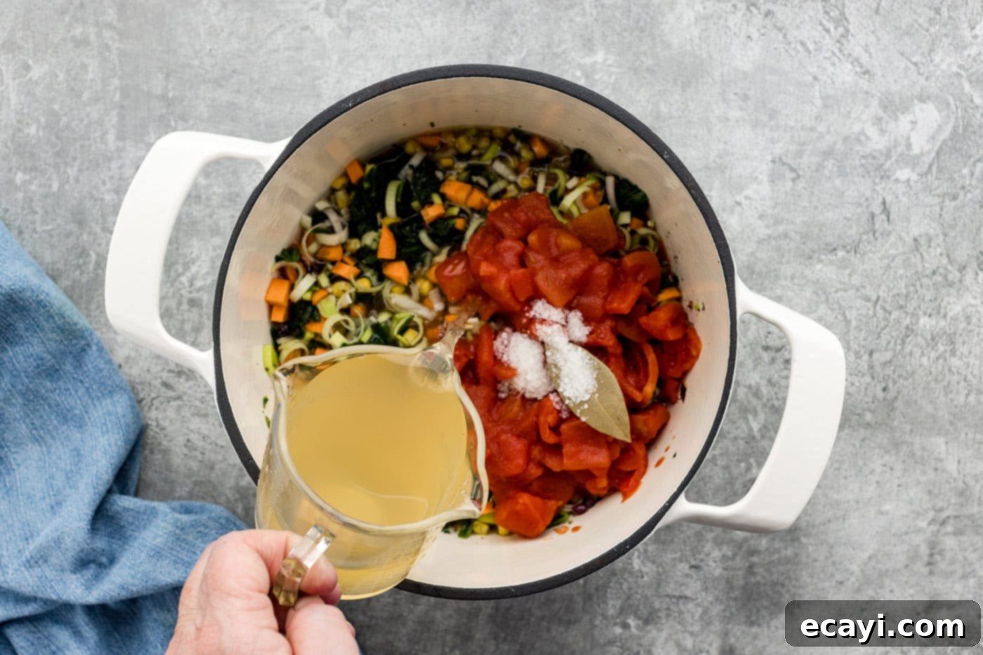 Hearty Veggie Rice Soup 8 hand pouring vegetable stock into pot with diced tomatoes, bay leaf, and sautéed vegetables