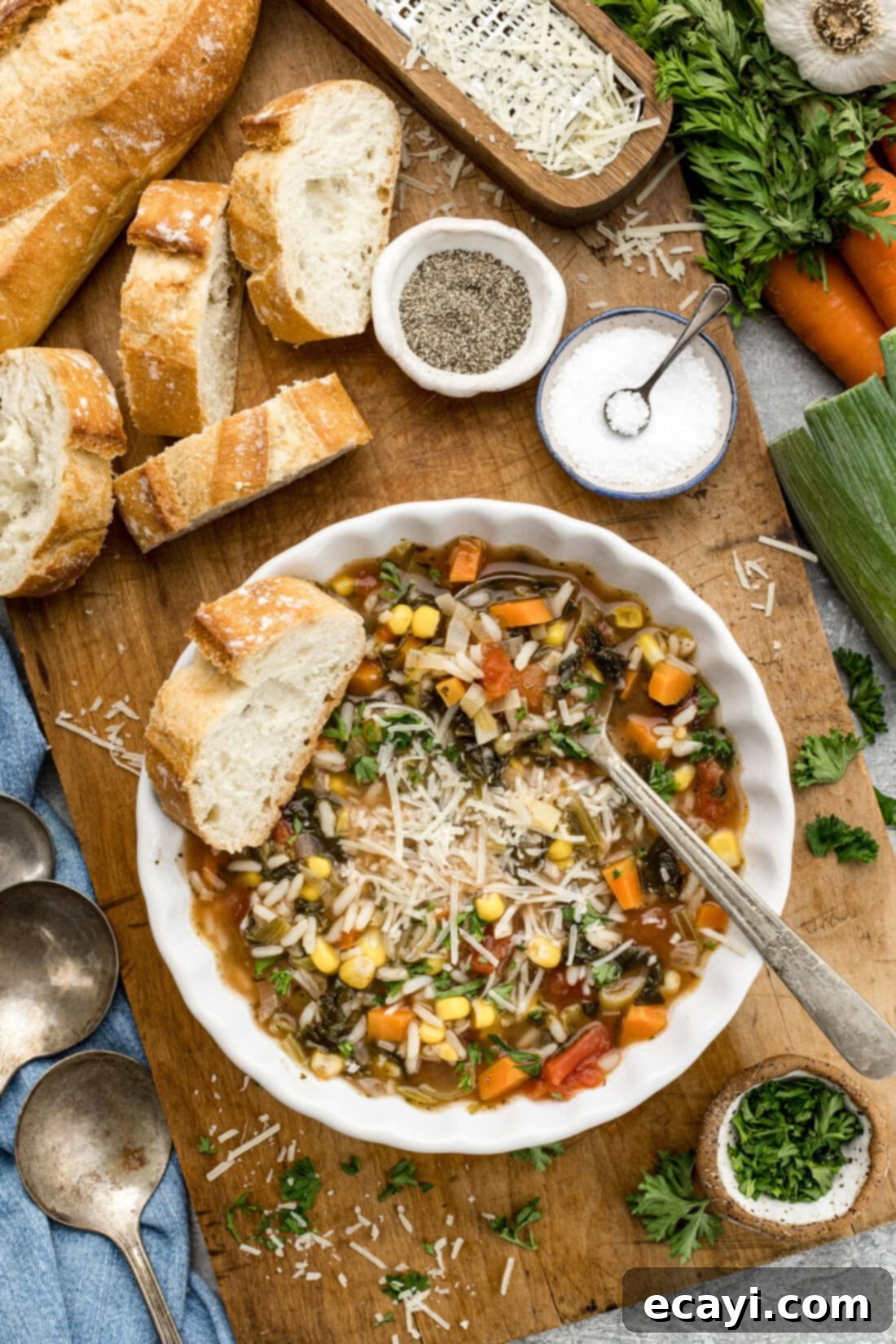 Hearty Veggie Rice Soup 10 Bowl of Vegetable Rice Soup surrounded by sliced bread, salt, pepper and fresh vegetables, ready to be enjoyed