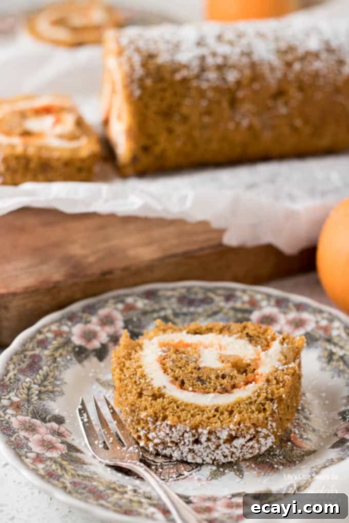 This Pumpkin Roll is a thin, moist pumpkin cake with or without walnuts, filled with a creamy frosting mixture and wrapped into a swirl of sweet heaven! A delicious slice of pumpkin roll cake artfully placed on a dessert plate, showcasing the elegant swirl of moist pumpkin cake and creamy frosting, dusted with powdered sugar.