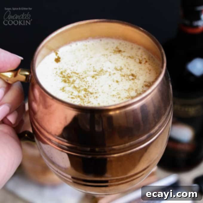 Homemade Eggnog Cocktail: A thick, rich, and flavorful holiday drink made with eggs, sugar, milk, cream, rum, and nutmeg. Perfect for your festive party. A close-up of a frothy, golden eggnog cocktail served in a gleaming copper mug, highlighting its rich texture and festive presentation.