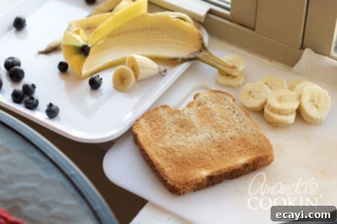 Making this bear toast is quick and simple, making it the perfect food-craft for kids in under 10 minutes! Step 1: Preparing banana slices and selecting blueberries of similar size for the Paddington Bear toast recipe.