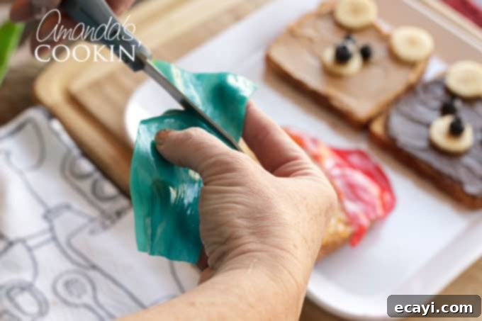 Making this bear toast requires minimal time and skill, making it the perfect food-craft to do with your kids in under 10 minutes! Detail of cutting red fruit roll-ups into the crescent and square shapes for Paddington's iconic hat on the toast.