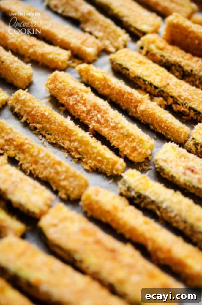 These Crispy Zucchini Fries are a healthy alternative to traditional French fries, but believe me when I say they don't compromise on flavor at all! #baked #dinnersides #snacks #healthysnacks #zucchini #sidedishes Crispy baked zucchini fries on pan, ready to be served as a healthy snack or side dish.
