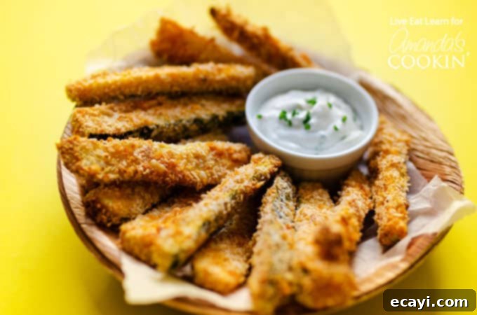 These Crispy Zucchini Fries are a healthy alternative to traditional French fries, but believe me when I say they don't compromise on flavor at all! #baked #dinnersides #snacks #healthysnacks #zucchini #sidedishes A serving of crispy baked zucchini fries alongside a small bowl of creamy gorgonzola dipping sauce, highlighting a perfect pairing.