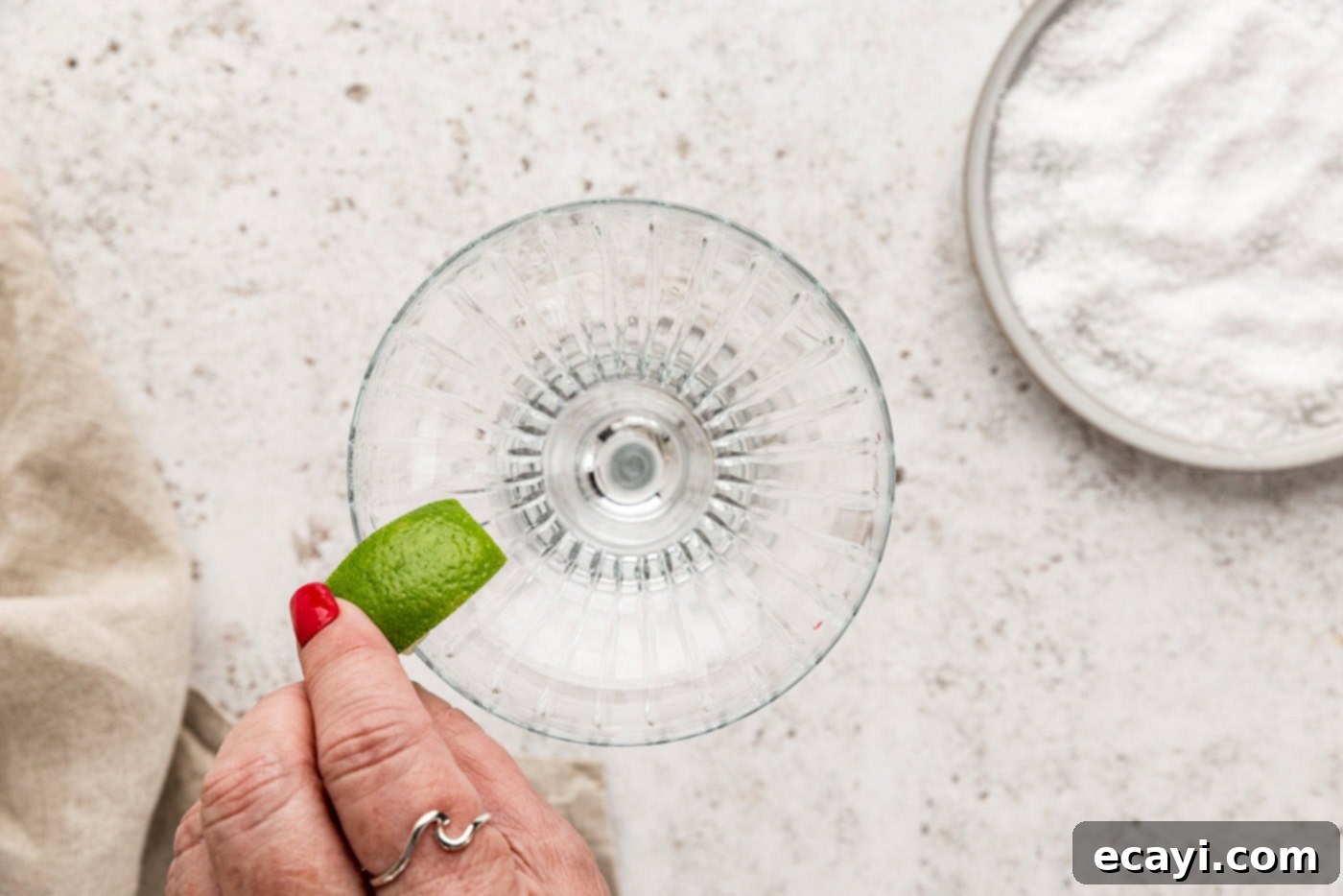 Berry Burst Margarita 8 A hand rubbing a fresh lime wedge around the rim of a margarita glass, preparing it for a salted rim.