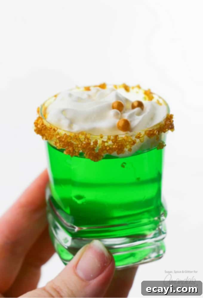 These Green Jello Shots with gold sugar rims and a dollop of whipped cream are perfect for St. Patrick's Day but are good for all summer long, too! #stpatricksday #jelloshots #jello #cocktails #summer #vodka #lime Holding Green Jello Shot