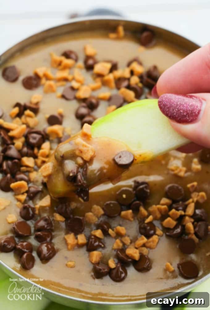 Luscious Caramel Apple Treat 3 Close-up of a crisp green apple slice being dipped into a silver bowl of homemade caramel apple dip, highlighting its smooth, rich texture.