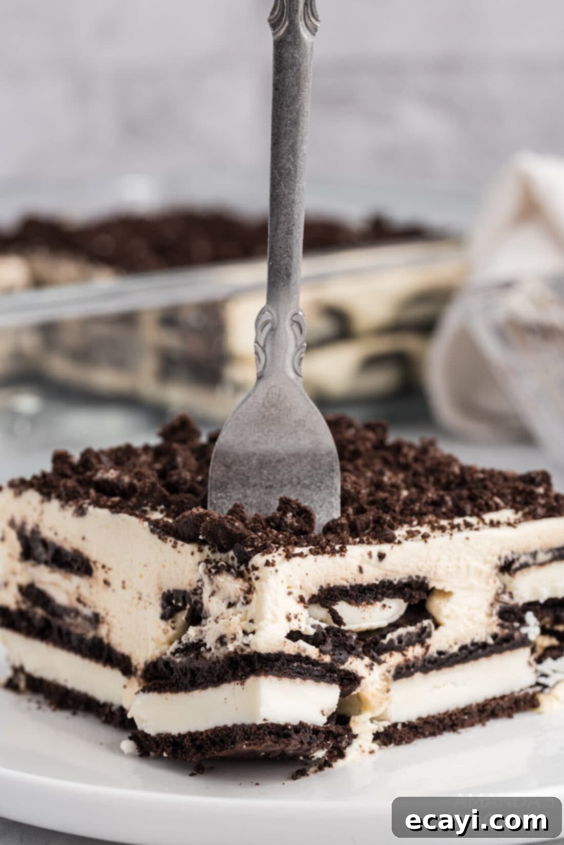 No-Bake Oreo Delight 3 A fork piercing into a piece of creamy Oreo Icebox Cake on a white plate, showcasing its soft layers.