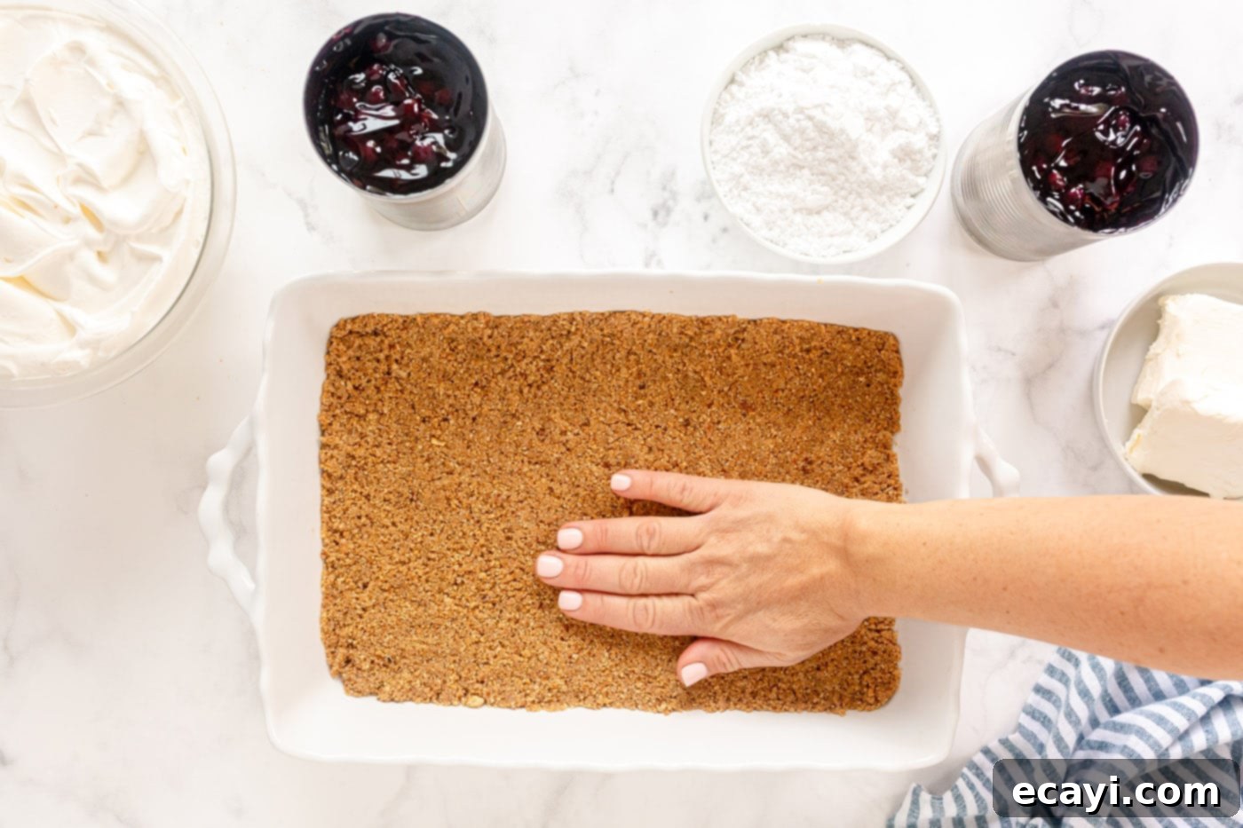 Blueberry Bliss 7 Hands firmly pressing the graham cracker and pecan crust mixture into the bottom of a 13x9 inch baking pan.