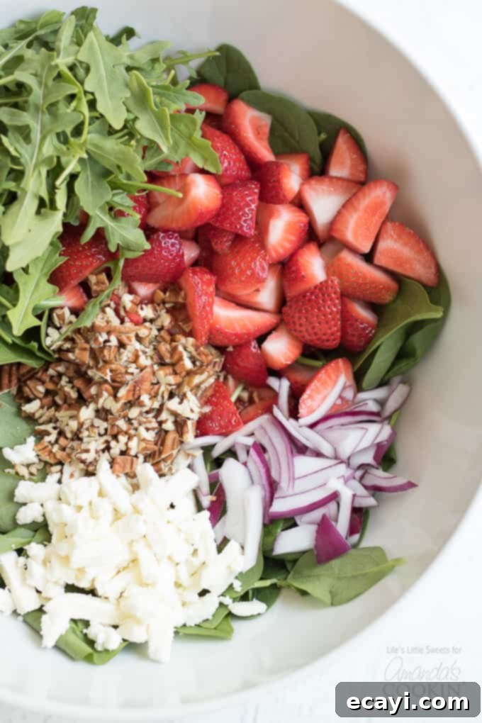 Vibrant Strawberry Salad 5 Close-up of fresh strawberries, finely sliced red onions, crunchy pecans, and vibrant spinach in a mixing bowl, prepped for the strawberry salad.
