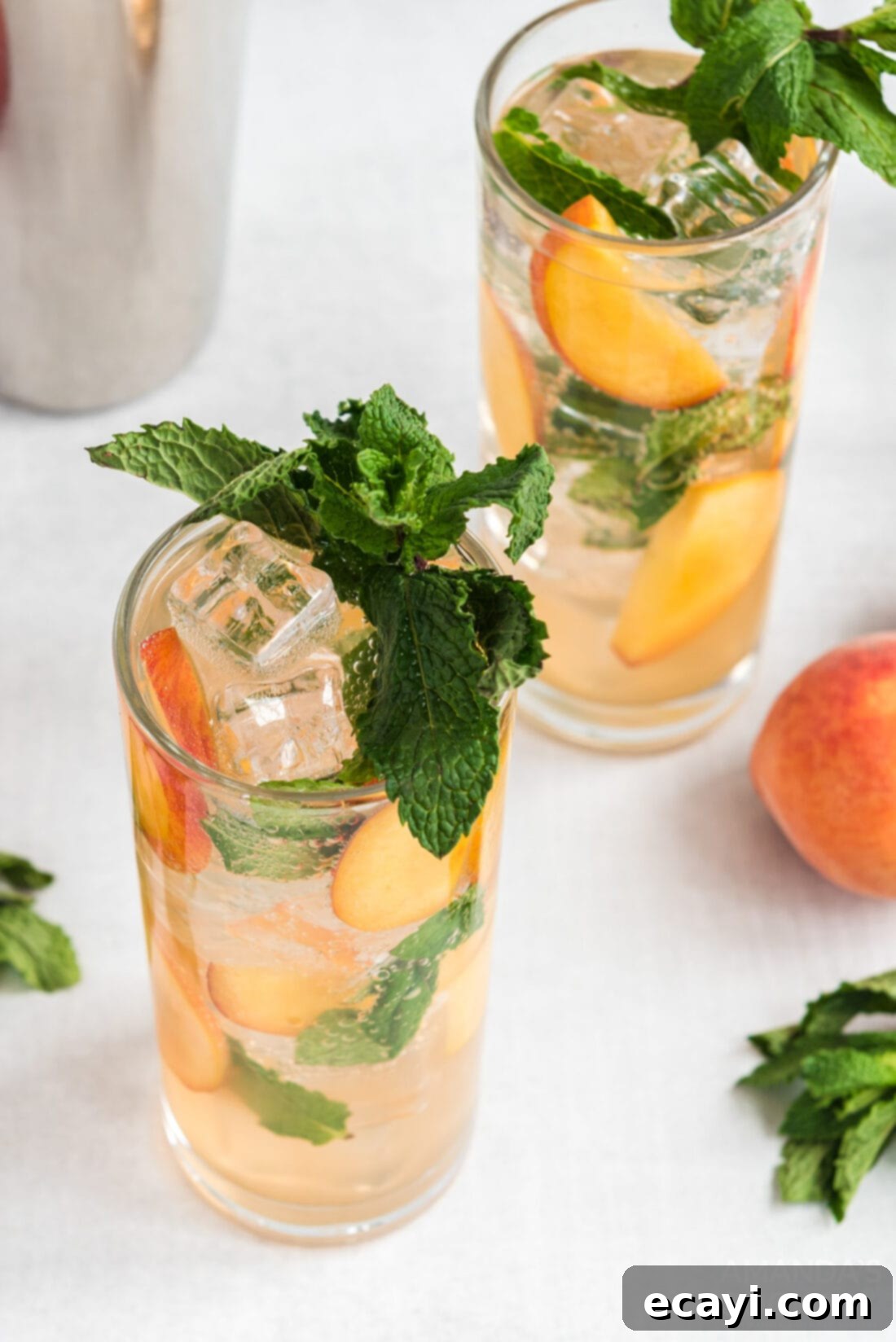 Peach Paradise Mojito 3 Two refreshing peach mojitos served in tall glasses, garnished with fresh mint and peach slices, sitting on a wooden surface.