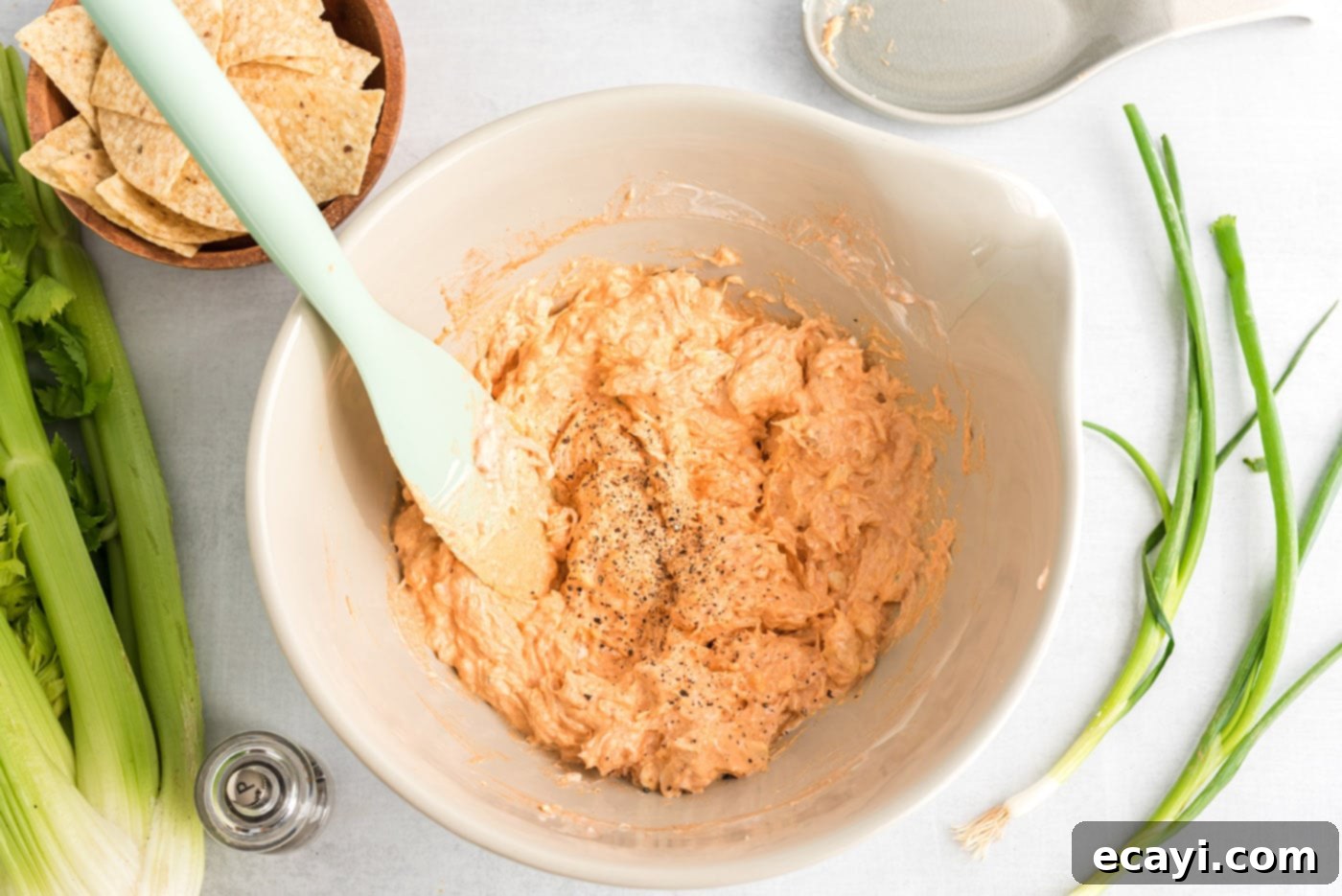 Ultimate Buffalo Chicken Dip 6 A rubber spatula actively mixing the buffalo chicken dip ingredients in a bowl, creating a smooth and creamy texture.